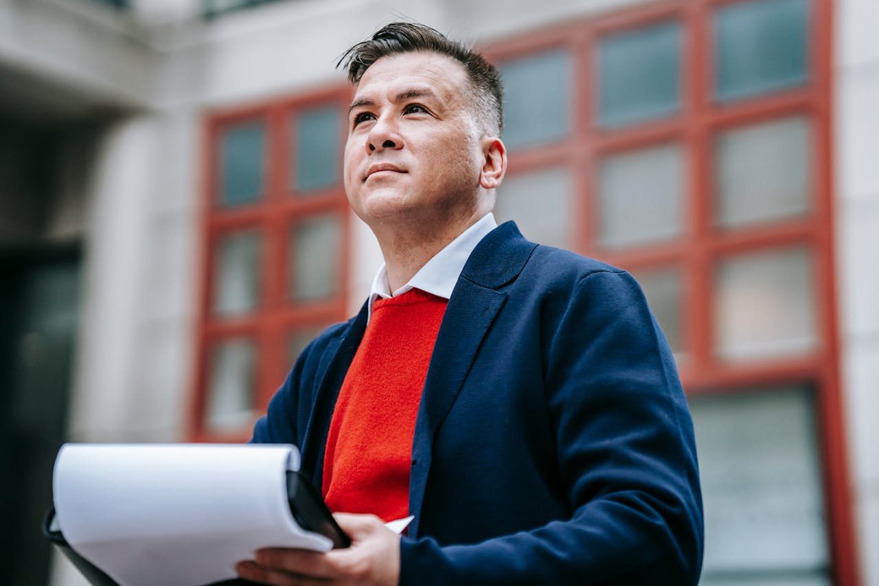 A confident businessman in a stylish outfit reviewing documents outdoors in a professional setting.